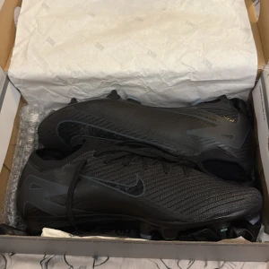 Nike svarta fotbollsskor med dobbar - Svarta mecurials elit fotbollsskor, dom är helt oanvända de är skruvdobbar/gräs också dom är i jätte bra skick, har aldrig använt dom heller plus de kommer med boxen,extraskruvdobbar ifall de andra skulle gå sönder eller liknande så går de att skruva fast nya bara sen även en skopåse som sagt dessa skor är i sprillans nyskick också