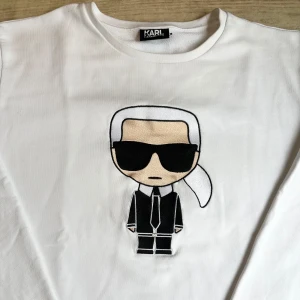 Vit sweatshirt från Karl Lagerfeld - Vit sweatshirt från Karl Lagerfeld med ikonisk broderad Karl-figur framtill. Tröjan har rund hals, långa ärmar och ribbade muddar. Tillverkad i mjuk bomull som är skön att bära. Perfekt för dig som gillar stilrena plagg med en twist.