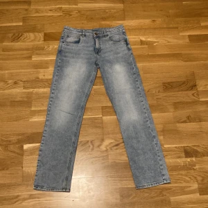 Ljusblå raka jeans i storlek 170 - Snygga ljusblå jeans med raka ben och klassisk femficksdesign. Jeansen har en enkel tvättad look och är tillverkade i mjukt denimtyg. Perfekta för dig som gillar en avslappnad och tidlös stil. Storlek 170. I ett mycket bra skick