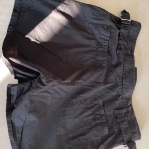Svarta shorts från Filippa K med spänne - Svarta shorts från Filippa K med snygga spänndetaljer i midjan och fickor både fram och bak. Klassisk rak modell i bomull, perfekt för en clean och stilren look. Passar dig som gillar minimalistisk design och vill ha något som funkar till många outfits.