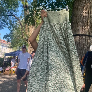 Grönmönstrad långkjol - Säljer en långkjol med smock upptill och ett grönt och vitt grafiskt mönster. Kjol har en luftig passform och är perfekt för varma dagar. Materialet känns som bomull och den har en bohemisk vibe.