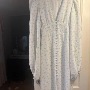 Vit blommig kortklänning med puffärm - En intresse koll på min superfina adoore postiano klänning. Superfin vit klänning med små blå och gröna blommor, markerad midja och v-ringning. Klänningen har puffiga långärmar och knappar framtill!🩵🩵🩵Klänningen är i nyskick! 