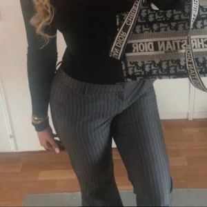 Grå kostymbyxor med smala ränder - Snygga grå kostymbyxor med smala vita ränder. Byxorna har en klassisk rak passform och är perfekta för en stilren look. Tillverkade i ett mjukt material som känns bekvämt hela dagen. Passar perfekt till både skjorta och t-shirt.