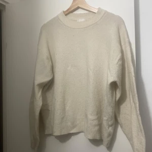 Beige stickad tröja i oversize - Mysig beige stickad tröja med rund halsringning och långa ärmar. Tröjan har en avslappnad, oversized passform och ribbade muddar vid ärmslut och nederkant. Perfekt för lager-på-lager under kyliga dagar.