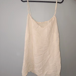 Linnetopp - Säljer en ljusbeige linnetopp med tunna axelband och avslappnad passform. Toppen är tillverkad i en mix av viskos och polyester, vilket ger ett mjukt och luftigt material. Perfekt för varma dagar och enkel att styla med jeans eller kjol. Aldrig använd!
