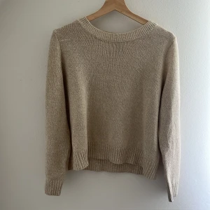 Beige stickad tröja från H&M Divided - En stilren beige stickad tröja från H&M Divided i storlek M. Tröjan har rund halsringning, ribbade muddar och är långärmad. Perfekt för lager-på-lager och enkel att matcha med jeans eller kjol.