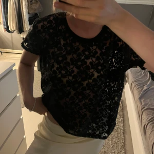 Svart blommig spetsblus - Superfin svart blommig spetsblus med korta ärmar. Blusen är transparent med ett snyggt blommönster och rund halsringning. Använd fåtal gånger ☺️