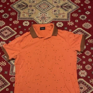 Orange pikétröja från Armani m - Snygg orange pikétröja från Armani Jeans i storlek m. Tröjan har bruna detaljer på krage och ärmslut samt små diskreta mönster över hela tyget. Tillverkad i mjuk bomull med lite stretch för extra komfort. Perfekt för dig som vill sticka ut med stil. Den passar bra på 170-180+