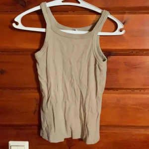 Beige topp från H&M - Säljer en beige topp från H&M i storlek S. Toppen har breda axelband och ärmlös design, perfekt för varma dagar. Enkel och stilren modell som är lätt att matcha med olika outfits.