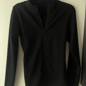 Svart ribbad jacka med dragkedja - Svart ribbad träningskofta med hel dragkedja framtill och lång ärm. Snygg och enkel.