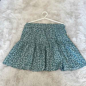 Blommig kortkjol från SHEIN - Supersöt kortkjol från SHEIN i grönt med vitt blommönster. Kjolen har volang och resår i midjan för en bekväm passform. Perfekt för dig som gillar en feminin och trendig stil. Materialet känns lätt och flowy, perfekt för varmare dagar. Passar även S