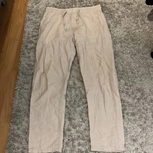Linnebyxor beige - Snygga beiga linnebyxor från Jack & Jones med avslappnad passform och elastisk midja med snörning. Byxorna har sidfickor och en bakficka med diskret logga. Perfekta för chill dagar eller när du vill ha en lätt och luftig stil.