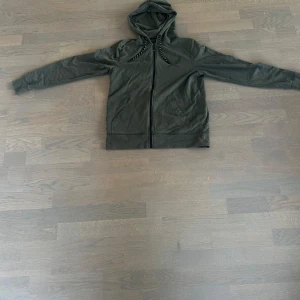 Mörkgrön hoodie med dragkedja och huva - Säljer en mörkgrön hoodie av märket SOC med dragkedja framtill och huva med snörning. Tröjan har långa ärmar och två fickor på magen. Perfekt för en chill och avslappnad stil. Materialet känns mjukt och bekvämt, 60% bomull 35% polyester och 5% elastan