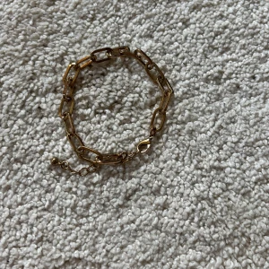 Chunky guldarmband med kedjelänkar - Snyggt armband i chunky stil med stora, rektangulära kedjelänkar i guldton. Justerbar längd med liten kula i änden. Perfekt accessoar för att lyfta din outfit med en trendig touch. OBS!!!! KOMMER GÖRAS RENT INNAN SICKAD