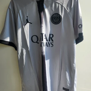 PSG Neymar Jr 10 fotbollströja vit - Snygg PSG fotbollströja i vitt med svarta detaljer, Neymar Jr och nummer 10 på ryggen. Jordan-logga på bröstet, Paris Saint-Germain-märke och sponsortryck. Tillverkad i lätt och ventilerande material, perfekt för match eller träning. Storlek Xl. Inte äkta!!