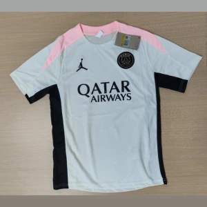 Priset diskuteras  - Snygg PSG fotbollströja i vitt med svarta och ljusrosa detaljer, kortärmad och tillverkad i lätt, ventilerande material. Matchande svarta shorts med rosa inslag och PSG-logga samt Jordan-logga. Perfekt för dig som vill sticka ut på planen.