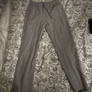 Randiga linnebyxor med snörning - Snygga grå linnebyxor med vita ränder och avslappnad passform. Byxorna har elastisk midja med snörning för extra komfort. Perfekta för chill dagar eller varma sommardagar. NYPRIS 300kr. MITT PRIS 150kr.                                                                                                         Aldrig använda. Storlek XS