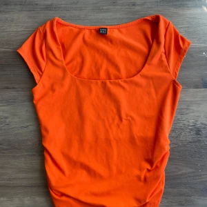 Orange topp med rynkade detaljer SHEIN - Snygg orange topp från SHEIN i storlek XS. Modellen har korta ärmar, fyrkantig ringning och coola rynkade detaljer i sidan. Perfekt för dig som vill sticka ut med en färgstark look. Tunn och mjuk bomullskänsla.