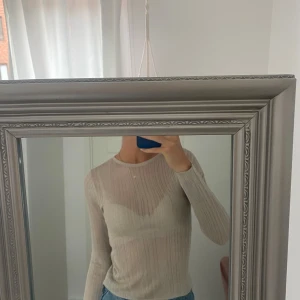 Beige ribbad långärmad tröja  - Säljer en tunn, ribbad och lätt transparent beige långärmad tröja från Anko. Tröjan har rund halsringning och sitter snyggt figurnära. Perfekt att styla med jeans eller kjol för en clean look.