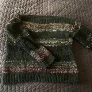 Randig stickad tröja från Nümph XS - Mysig stickad tröja från Nümph i gröna toner med inslag av vinrött, beige och guldiga metallictrådar. Tröjan har ett randigt mönster, lång ärm och en lite fluffig känsla tack vare mohair och ullblandning. Perfekt för dig som gillar en unik och färgstark look.