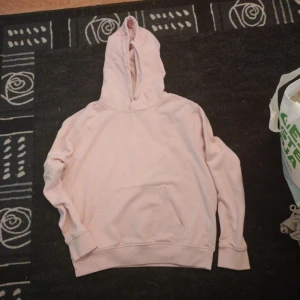 Ljusrosa hoodie med ficka - Mysig ljusrosa hoodie med stor huva och klassisk magficka. Tröjan har långa ärmar och breda muddar vid ärmslut och nederkant. Perfekt för chill dagar eller när du vill ha en enkel och stilren look.