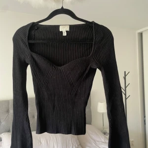 Svart ribbad topp från H&M - Svart långärmad ribbad topp från H&M i storlek S, med markerad byst och hjärtformad urringning. Den har stretchigt material och är använd men ändå i mycket bra skick.
