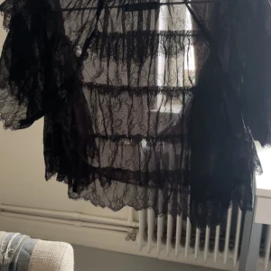 Svart spetsig bolerotopp med volang - Säljer en svart bolerotopp i transparent spets med volangdetaljer. Toppen har korta ärmar och är croppad, perfekt att slänga över ett linne eller klänning för en extra touch. Spetsen har ett fint mönster och ger en riktigt edgy vibe.