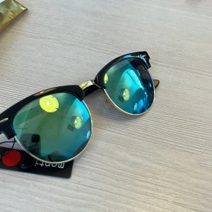 Svarta solglasögon med blå spegelglas - Snygga solglasögon med svart båge och guldiga detaljer. Glasen är blåtonade och spegelblanka, vilket ger en cool och modern look. Perfekta för att sticka ut i sommarvärmen. Helt oanvända