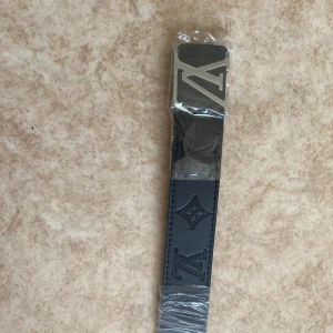 Svart L bälte med silver logga - Snyggt svart bälte med silver logga 110cm