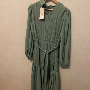 Hell ny Ljusgrön långklänning med knytband - Säljer hell ny, Superfin ljusgrön långklänning med plisserade detaljer och knytband i midjan. Klänningen har långa ärmar med lätt puff och en avslappnad passform. Perfekt för dig som gillar en romantisk och trendig stil. Storlek M/L