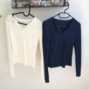 Två ribbade långärmade toppar - Säljer två likadana långärmade ribbade toppar med knappar framtill där uppe. En är i krämvit och den andra i marinblått. Den krämvita är lite genomskinlig men sålänge man har en vit bh så syns de inte som man ser iallafall. Dom är S men dom är väldigt stretchiga så dem passar från XS till M