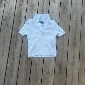 Ljusblå ribbad pikétröja BikBok XS - Supersöt ljusblå pikétröja från BikBok i ribbat material med små hålmönster. Tröjan har korta ärmar, klassisk krage och knappar framtill. Perfekt till jeans eller kjol för en fräsch look.