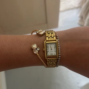 Klocka - Snygg klocka från Regal med rektangulärt ur och klassisk länk i  rostfri metall. Vit urtavla med romerska siffror och diskreta visare. Perfekt accessoar för att lyfta din outfit med en elegant touch.
