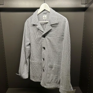 Randig overshirt från John Henric - Säljer en stilren overshirt från John Henric i vitt och blått med smala vertikala ränder. Jackan har klassisk krage, stora knappar framtill och två rejäla fickor. perfekt för sommar och vår. Fungerar både till vardag och fest. Helt ny!