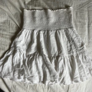 Vit volangig kjol - Supersöt vit kjol som kan användas även som tubtopp med smock upptill och två lager volanger nedtill. Kjolen har en luftig, flowy känsla som passar perfekt till varma dagar. 