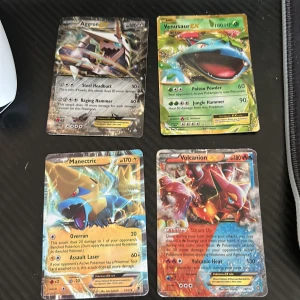 Pokémon EX-kort: Aggron, Venusaur, Manectric, Volcanion - Fyra coola Pokémon EX-kort med grymma illustrationer: Aggron, Venusaur, Manectric och Volcanion. Perfekt för dig som vill boosta din samling eller spela med vänner! Kortens skick varierar, se bilder för detaljer. Allihopa är bra skick förutom Manectric som är sämre skick. Skriv vid frågor.