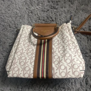 Väska - HElt ny!  Snygg axelväska från Gallantry Paris i beige och brunt med logomönster och randiga detaljer i mitten. Väskan har både handtag och axelrem, flera fack och dragkedja. Materialet är syntet med skinnliknande detaljer. Perfekt för dig som vill ha en trendig och rymlig väska.