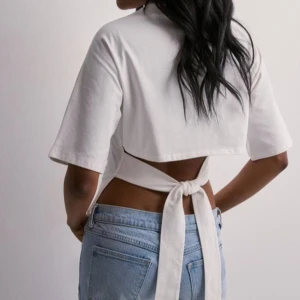 Vit topp med knyt från Nelly - Superfräsch vit croppad topp med korta ärmar och snygg knytning i ryggen. Perfekt till jeans eller kjol för en trendig look. Toppens material känns mjukt och lätt, och den öppna ryggen ger en cool twist. Använd två gånger 