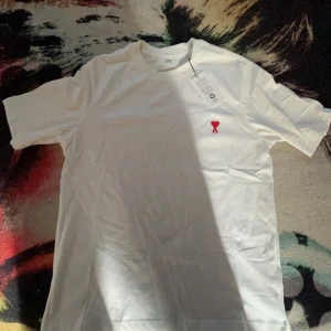 Ami Paris t-shirt helt ny! - Snygga t-shirts från Ami Paris med klassisk passform och kort ärm. Finns i både vit och marinblå, båda med det ikoniska röda hjärtemblemet broderat på bröstet. Tillverkad i mjuk bomull som känns skön mot huden. Perfekt för dig som gillar stilrena och trendiga plagg. 299 gör 1!