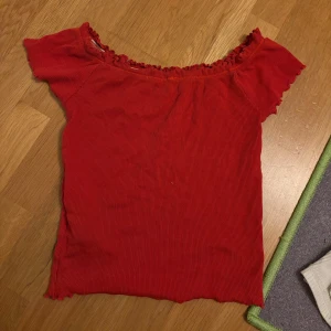 Röd ribbad offshoulder topp - Snygg röd ribbad topp med offshoulder-modell och korta ärmar. Toppen har volangkant vid halsringningen och nertill, vilket ger en extra söt touch. Perfekt att matcha med jeans eller kjol för en trendig look.