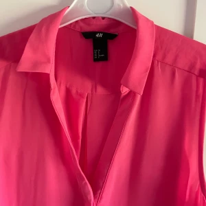 Rosa ärmlös blus från H&M - Säljer en snygg rosa ärmlös blus från H&M. Blusen har klassisk krage och v-ringning framtill, perfekt för en fräsch och stilren look. Lätt och luftig modell som passar till många olika outfits.