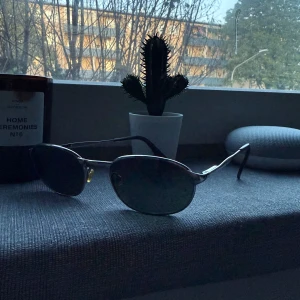 Ray-Ban ovala solglasögon i metall rb3003 - Snygga Ray-Ban solglasögon med ovala, mörka linser och tunna metallbågar i silver. Klassisk design med näskuddar i gult och svarta skalmar. Perfekta för dig som vill ha en stilren och vintage look. Nypris ligger på ca 1299 kr. 