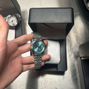  automatisk omega klocka med turkos urtavla - Snygg klocka från Pagani Design med en glansig turkos urtavla och klassiska romerska siffror. Boetten och länken är i silverfärgat rostfritt stål. Automatisk rörelse syns genom baksidan. Perfekt accessoar för dig som gillar stilrena detaljer.