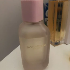 Zara Cashmere Rose parfym - Zara Cashmere Rose parfym i en frostad glasflaska med mjuka former och en ljusrosa kork. Flaskan har en stilren design med guldtext på framsidan. Perfekt för dig som gillar eleganta och feminina dofter. 100ml