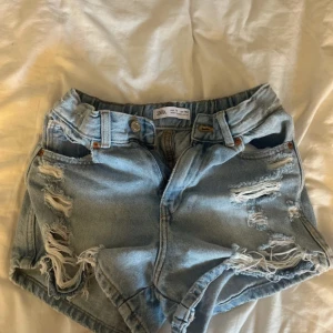 Ljusa jeansshorts från Zara med slitningar - Snygga ljusblå jeansshorts från Zara med råa, slitna detaljer och fransar. Klassisk femficksmodell med elastisk midja och knappstängning. Perfekta för sommardagar när du vill ha en avslappnad och trendig look. Storleken är 10Y Men skulle verkligen säga att de är stora i storleken, iaf i låren. Jag är 14 år och midjan är lite för liten på mig och låren är bra. Fint skick, knappt använda. 