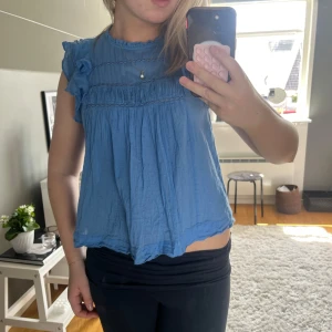 Blå volangtopp - Supersöt blå blus med volangdetaljer på axlarna och fina spetsinslag framtill. Blusen är luftig, perfekt för en chill och somrig look. Rund halsringning och ärmlös design med extra volym vid axlarna. Använd få gånger, nypris runt 600, hör av dig vid frågor💕