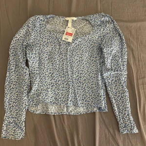Blommig blå och vit blus  - Supersöt blus från H&M i blått och vitt med småblommigt mönster. Långärmad modell med rundad halsringning och lätt transparent tyg. Perfekt för dig som gillar romantisk och fräsch stil.