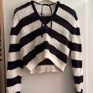 Randig Stickad Hoodie - Stickad hoodie från Zara med breda mörkblåa (nästan svarta) och vita ränder. Tröjan har lång ärm, v-ringning med snörning och luva. Den är virkad i ett luftigt material och har ribbade muddar vid ärmslut och nederkant. Använd en gång inga defekter, storlek M Nypris: 350kr