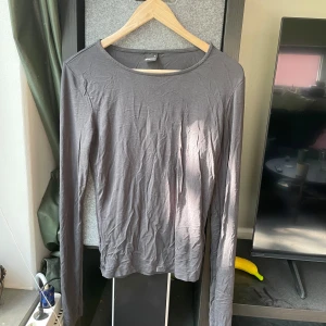 Grå långärmad topp från Gina Tricot - En basic grå långärmad topp från Gina Tricot i 95% viskos och 5% elastan. Enkel och stilren med rund halsringning och normal passform. Perfekt att styla lager på lager eller som den är till jeans eller kjol.