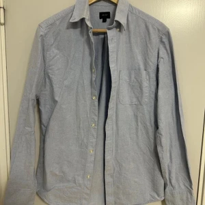 Ljusgrå skjorta  - Klassisk ljusgrå skjorta  med lång ärm, bröstficka och knappar framtill, perfekt för en clean och stilren look.